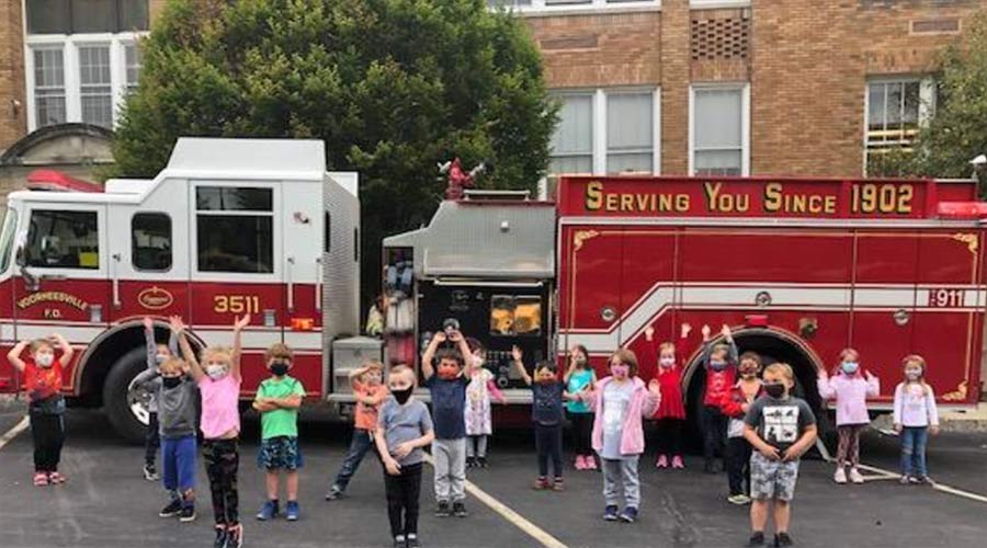 young students in masks standing in front of a fire truck