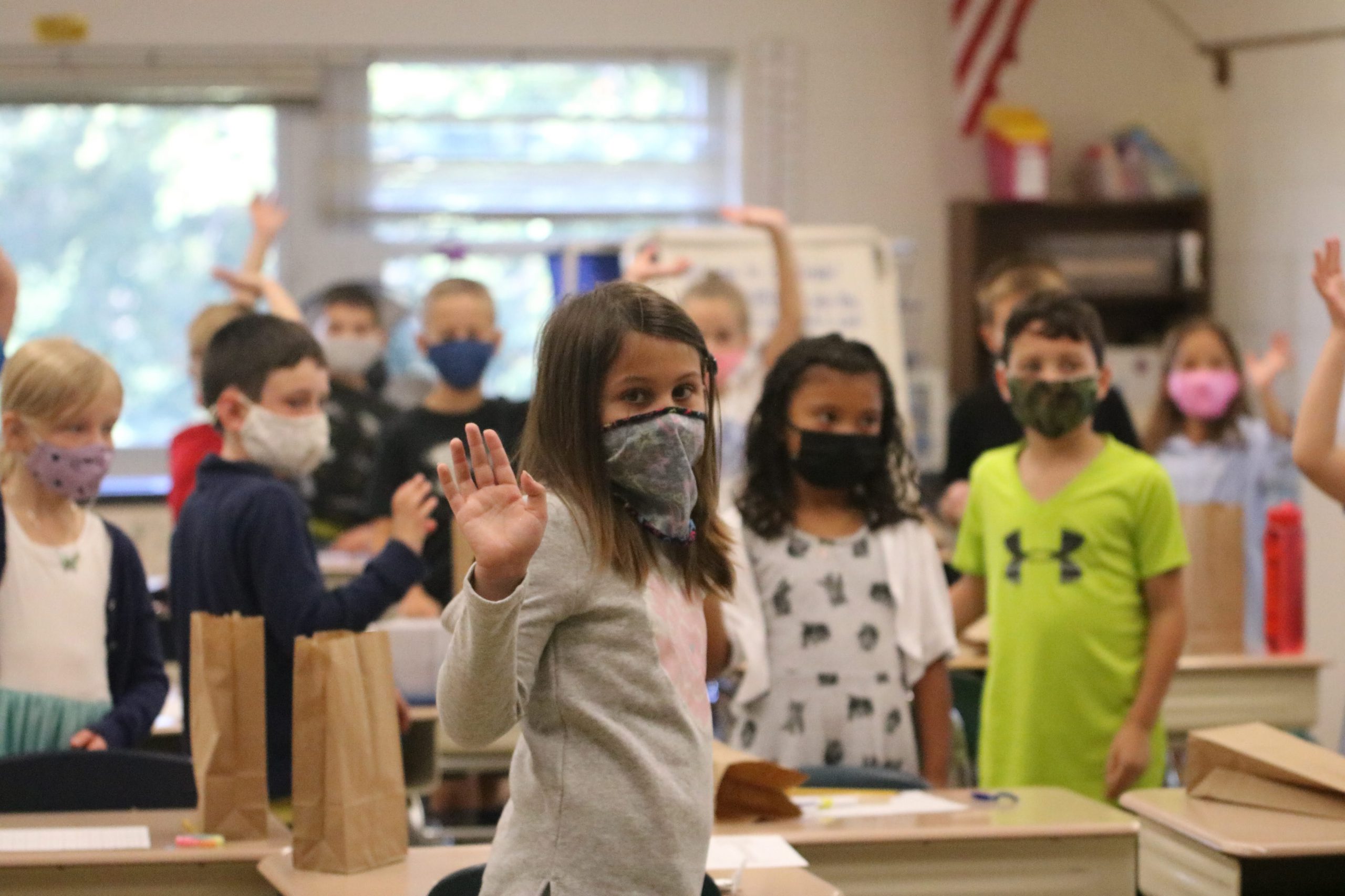 students standing in a classroom raising their hands