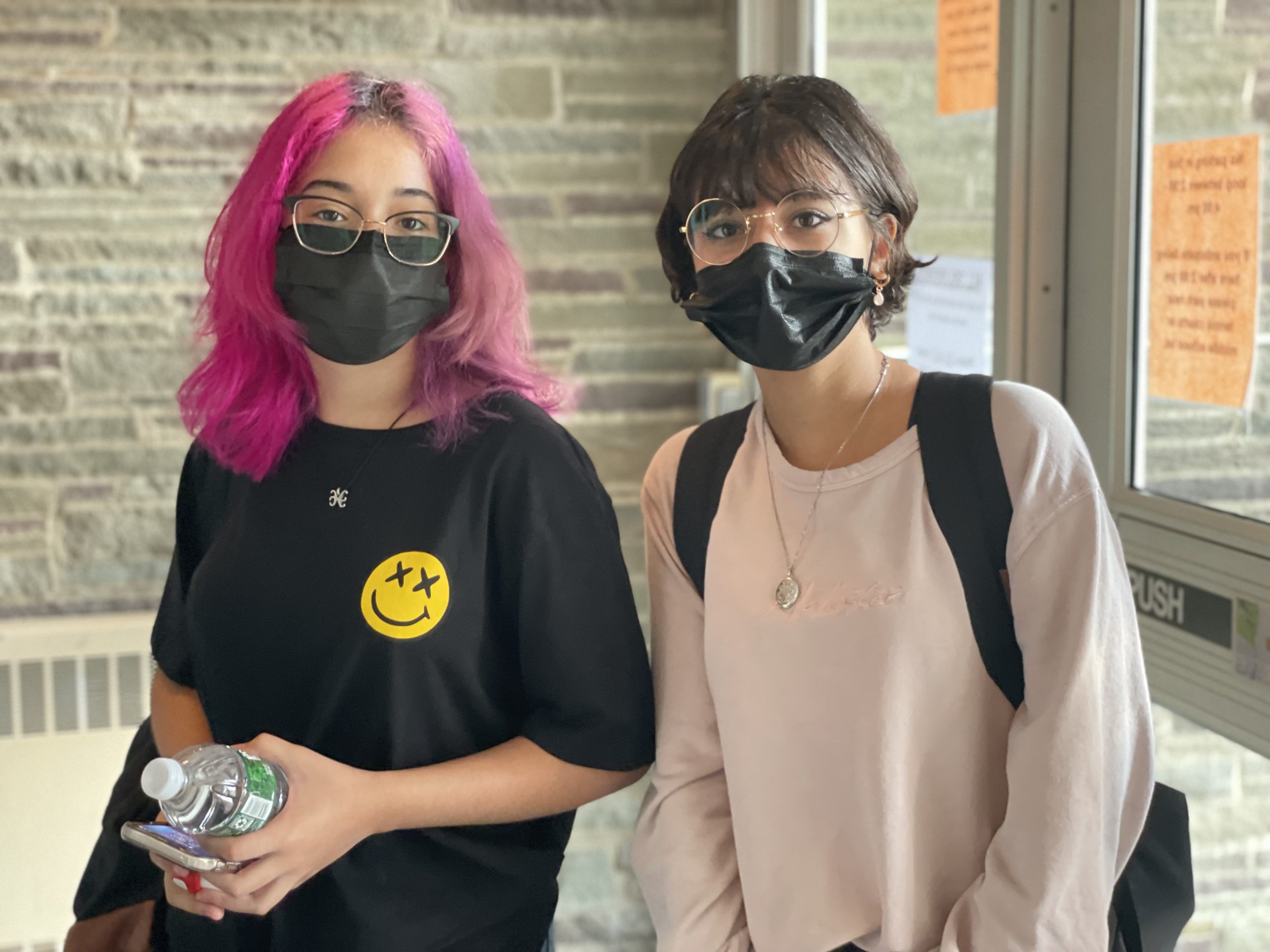 student with pink hair and other with black hair walking into school