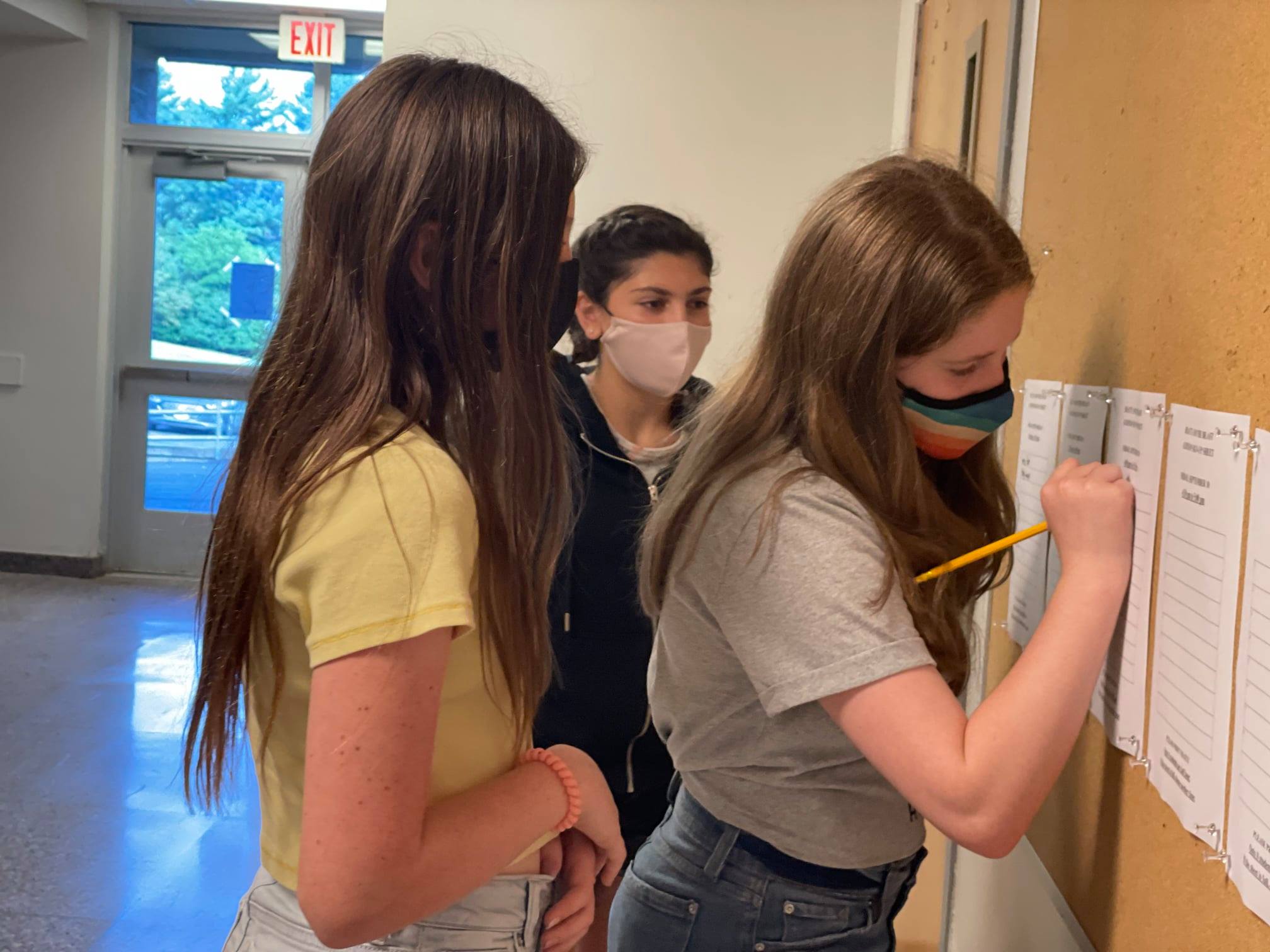 students signing up for a play on a form located on a wall