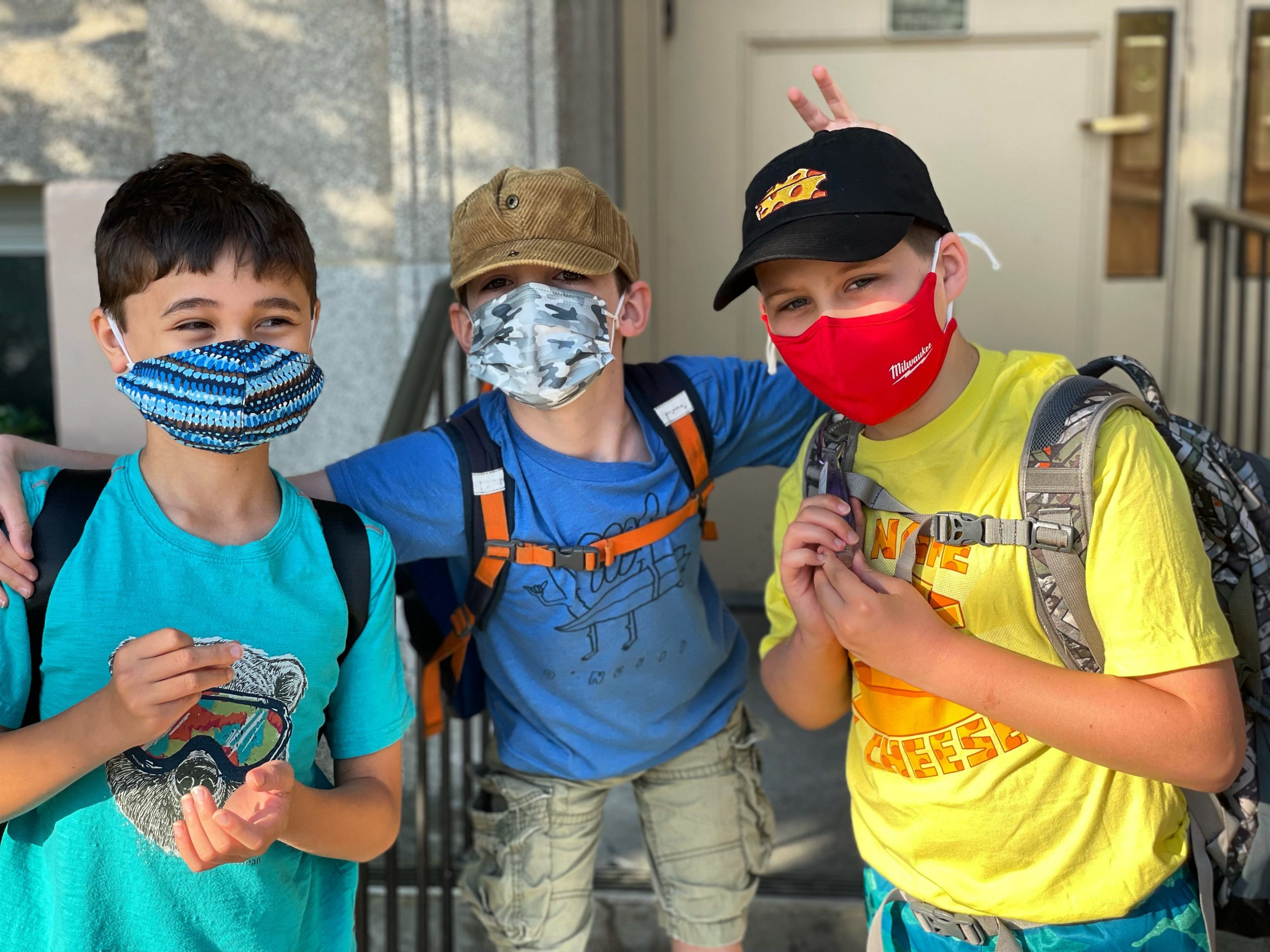 three students standing together and the one in the middle is giving bunny ears to his friends