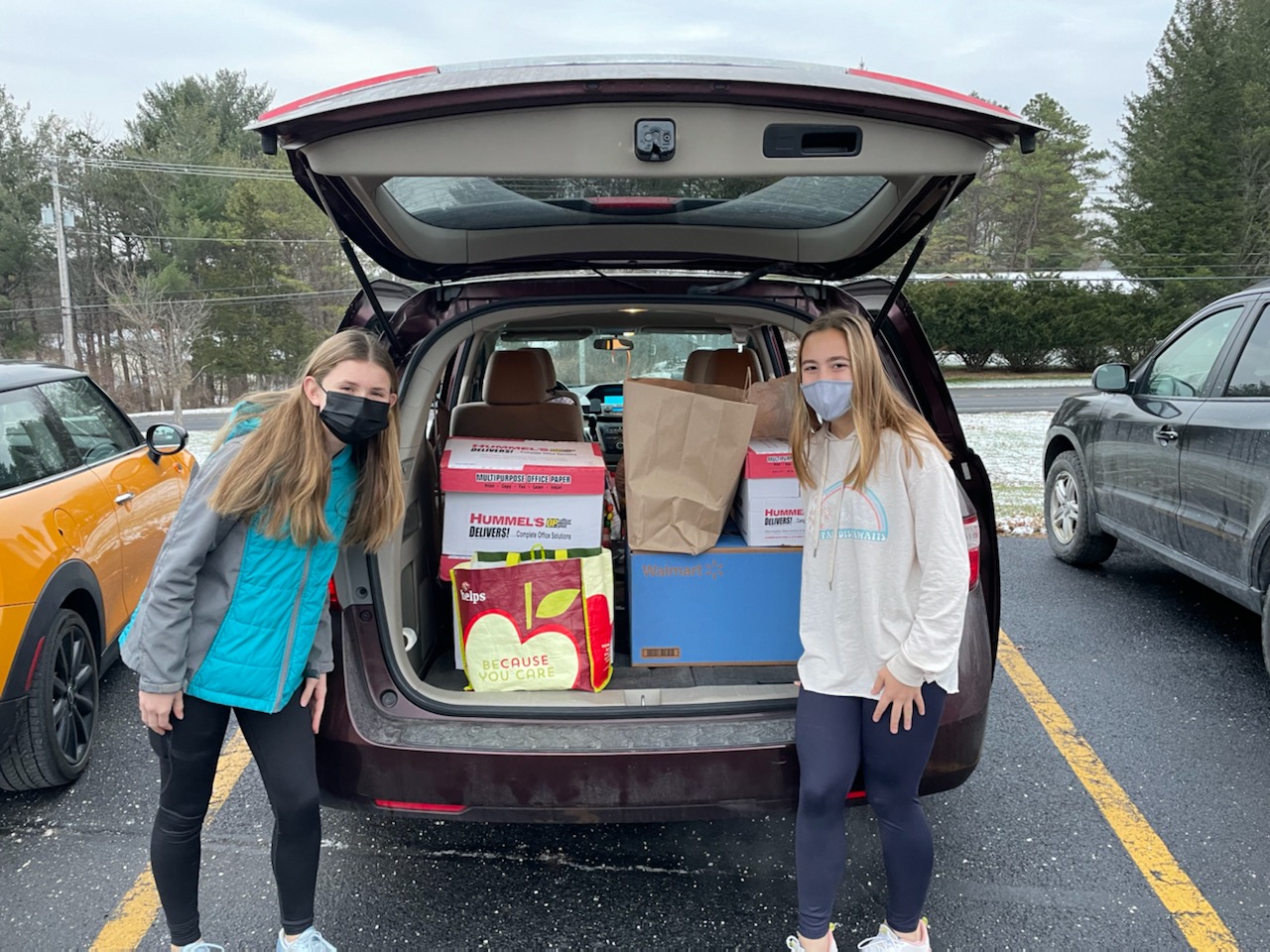 minivan hatch open with boxes of gifts inside and a student on each side