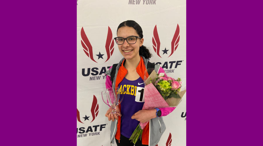 Teen holds winning cup and flowers. She is wearing a Voorheesville shirt and is smiling at the camera.