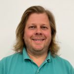 man with shoulder length hair and beard wearing a teal shirt