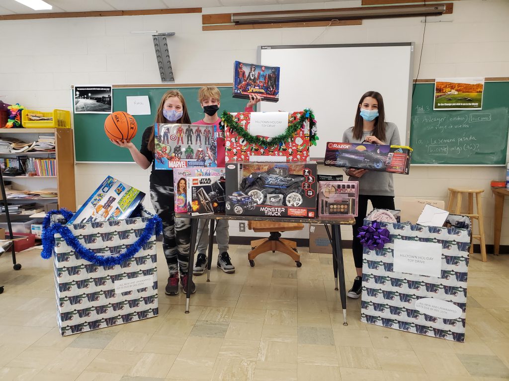 Three students holding balls and games and standing around numerous wrapped presents