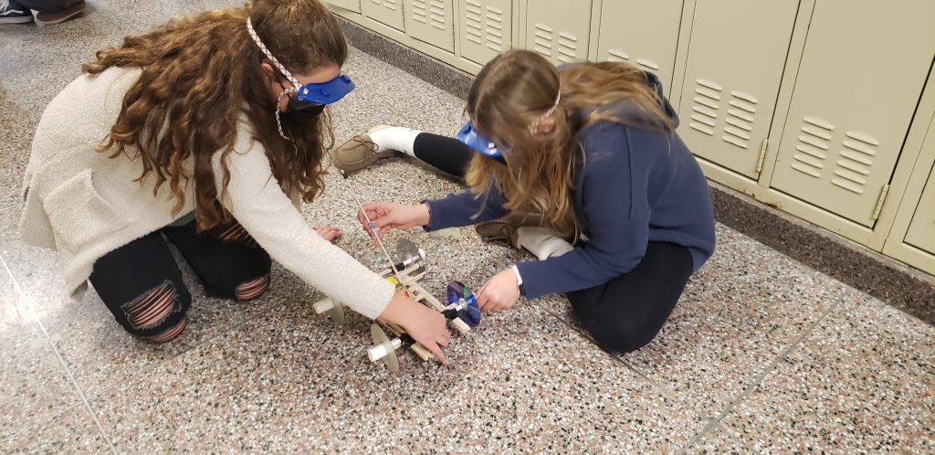 students trying out mousetrap cars on the floor of school