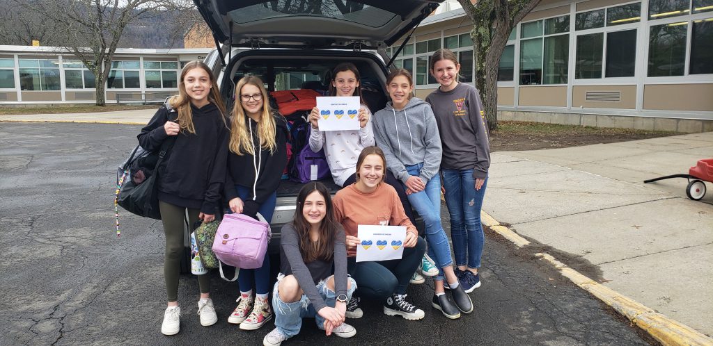 seven students standing in the back of an SUV filled with supplies for Ukraine