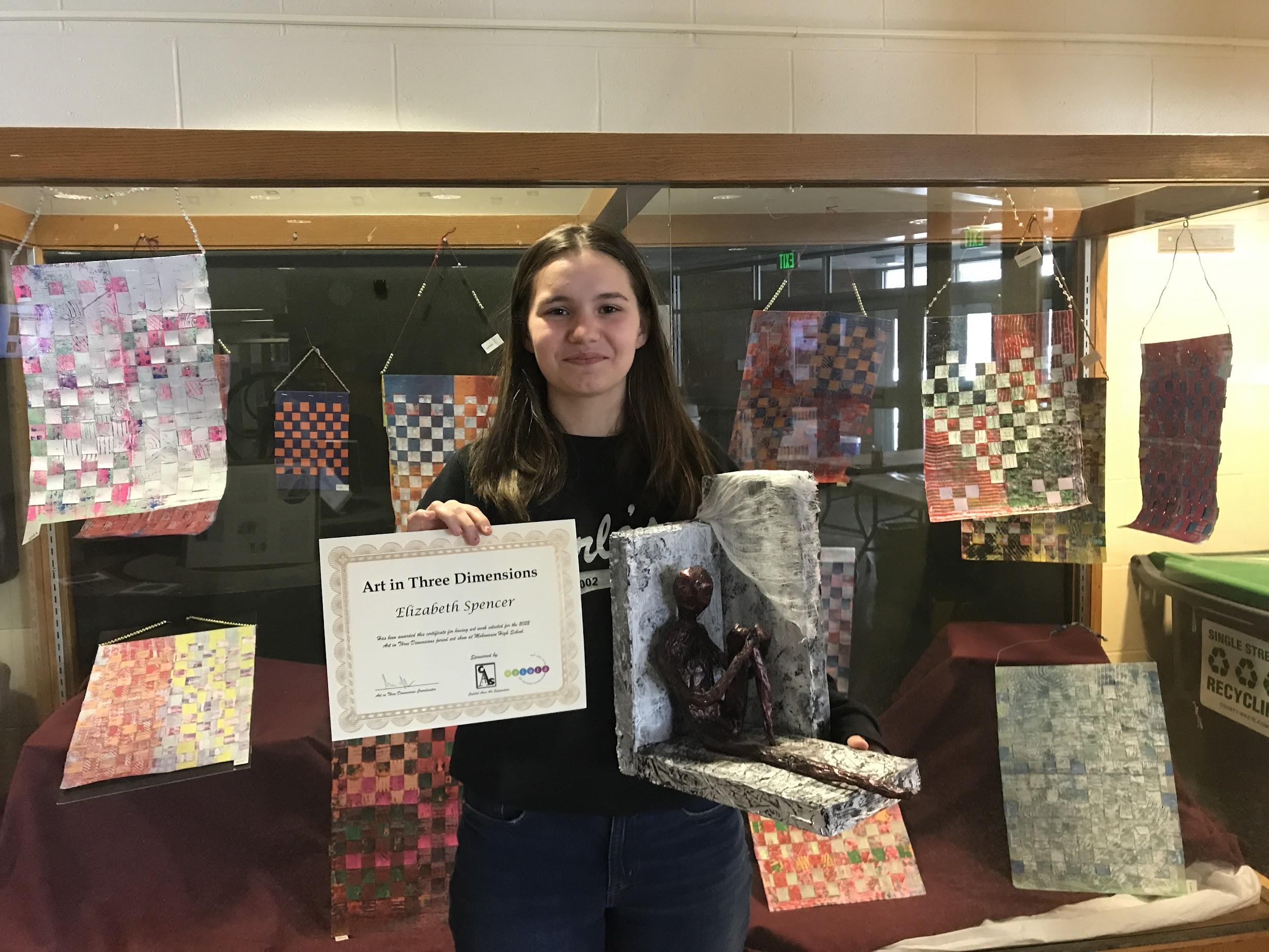 student holds up certificate and artwork