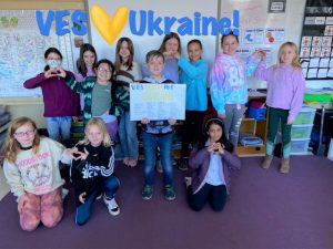 students stand together holding posters and flashing heart signs for Ukraine