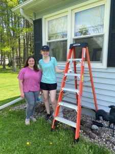 two students standing near a home with an open ladder