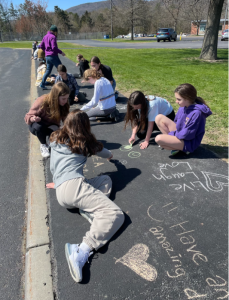 10 students sitting on sidewalk making chalk drawings on a sunny day