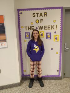 A middle school girl stands in front of the Star of the Week bulletin board.