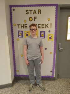 A middle school student stands in front of a Star of the Week bulletin board in a hallway