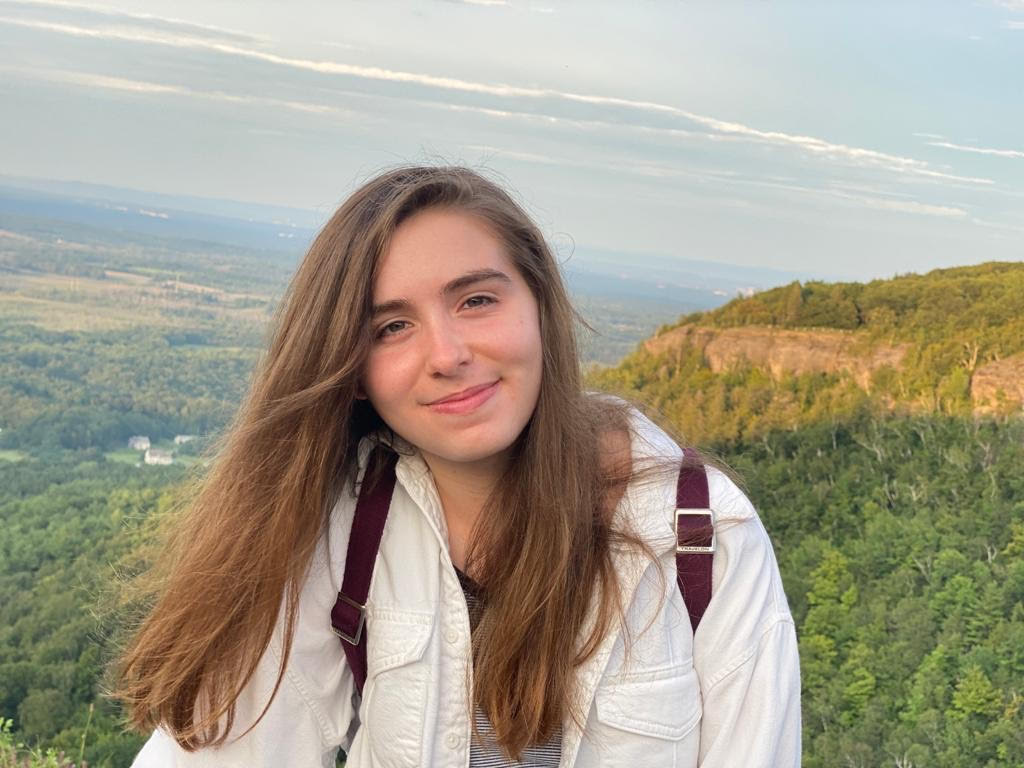 student wearing a backpack standing on a mountain with long flowy hair