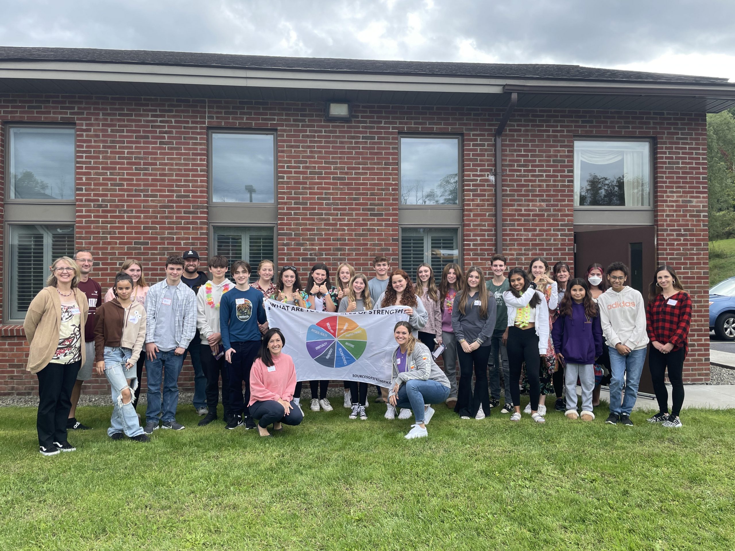 A group of highschoolers pose for a group photo outside in front of a brick school building