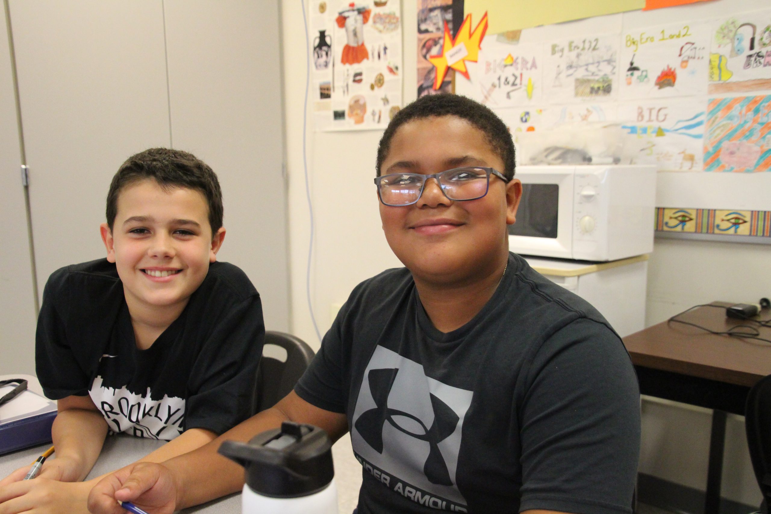 Two middle school students pose for a photo at their desk