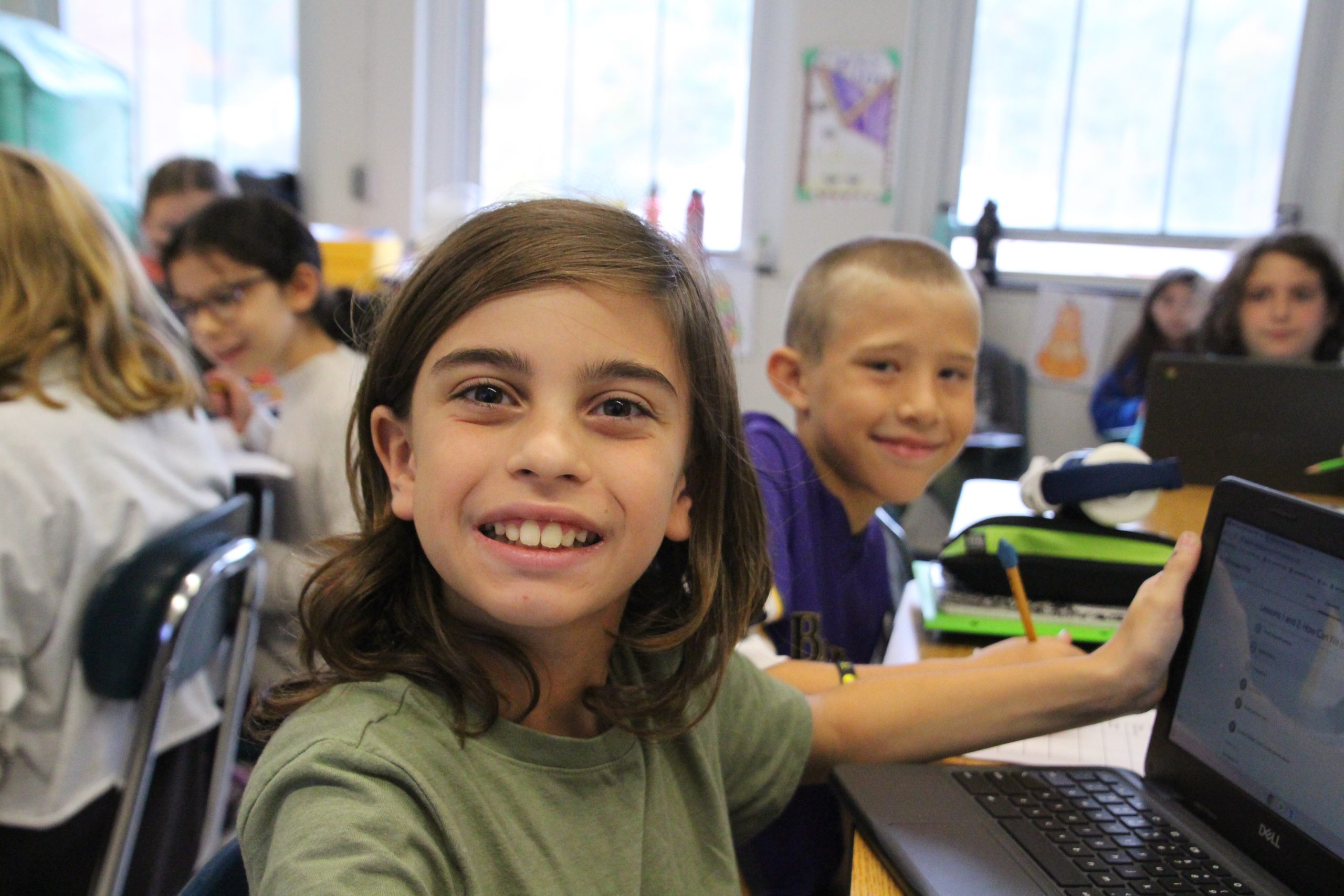 An elementary student smiles for a photo at their desk