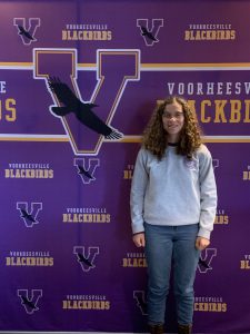 High schooler Julia Young stands in front of a Voorheesville logo wall