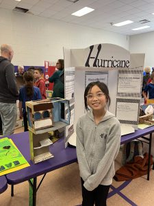 A 4th grade student stands in front of a project about hurricanes.