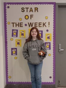 Girl stands in front of Star of the Week Banner.