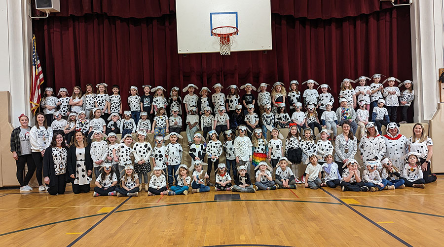 Over 75 kindergarten students are dresses as Dalmatians. They are sitting with their teachers and looking toward the camera.