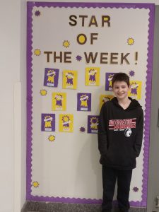 Boy stands in front of Star of the Week bulletin board.