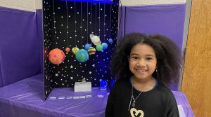 Child stands next to a science fair display about the planets for slider
