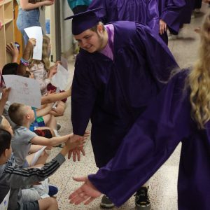 Student in cap and gown taps hands with young students