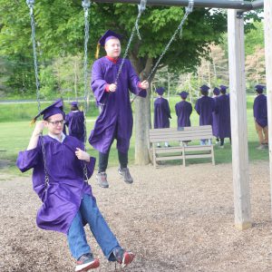 Students in cap and gown on swings