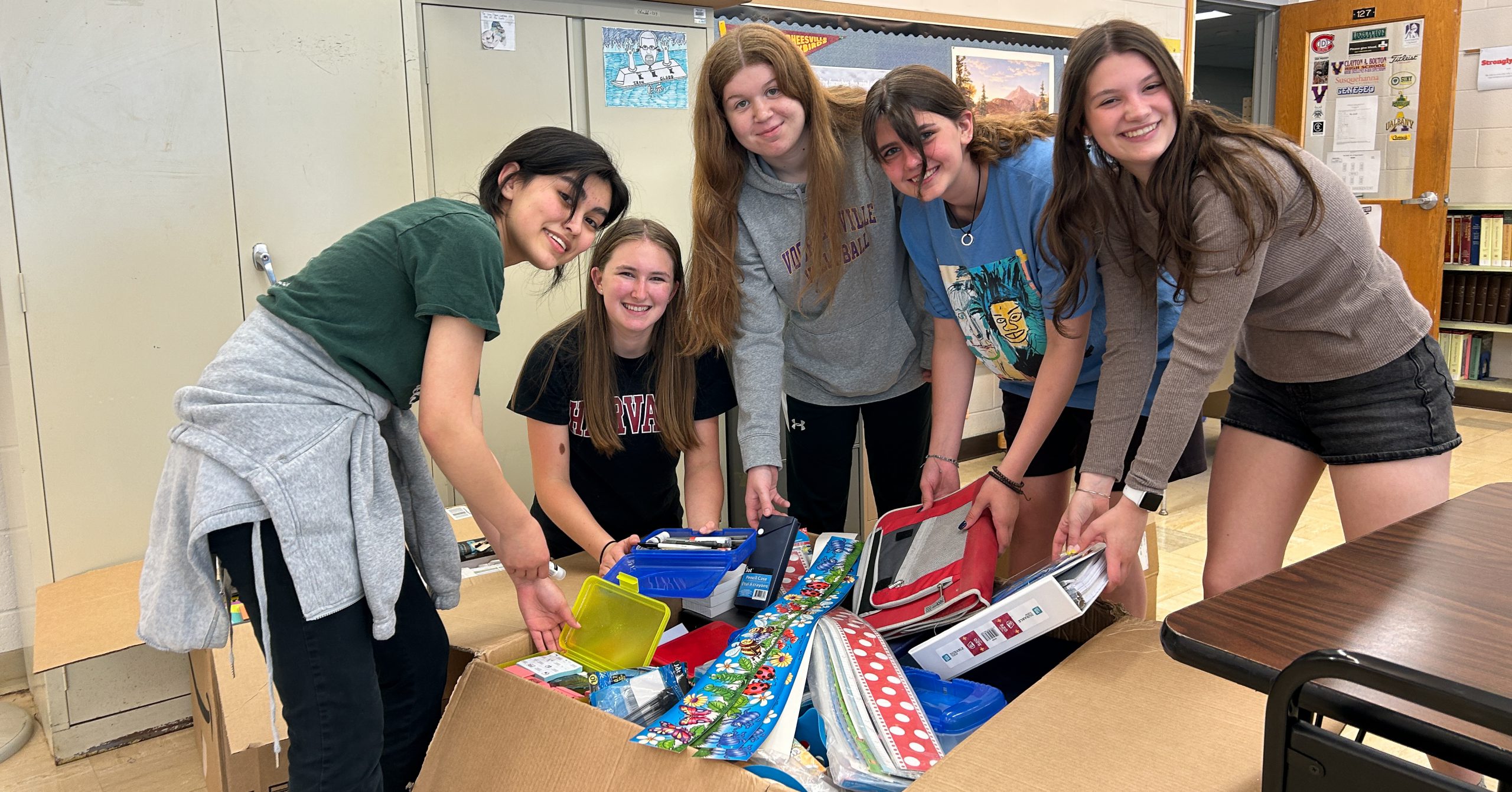 Five students surround a box of school supplies.