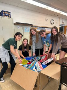 Five students stand next to large box of school supplies.