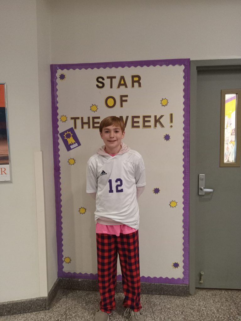 Ian stands in front of Star of the Week bulletin board.