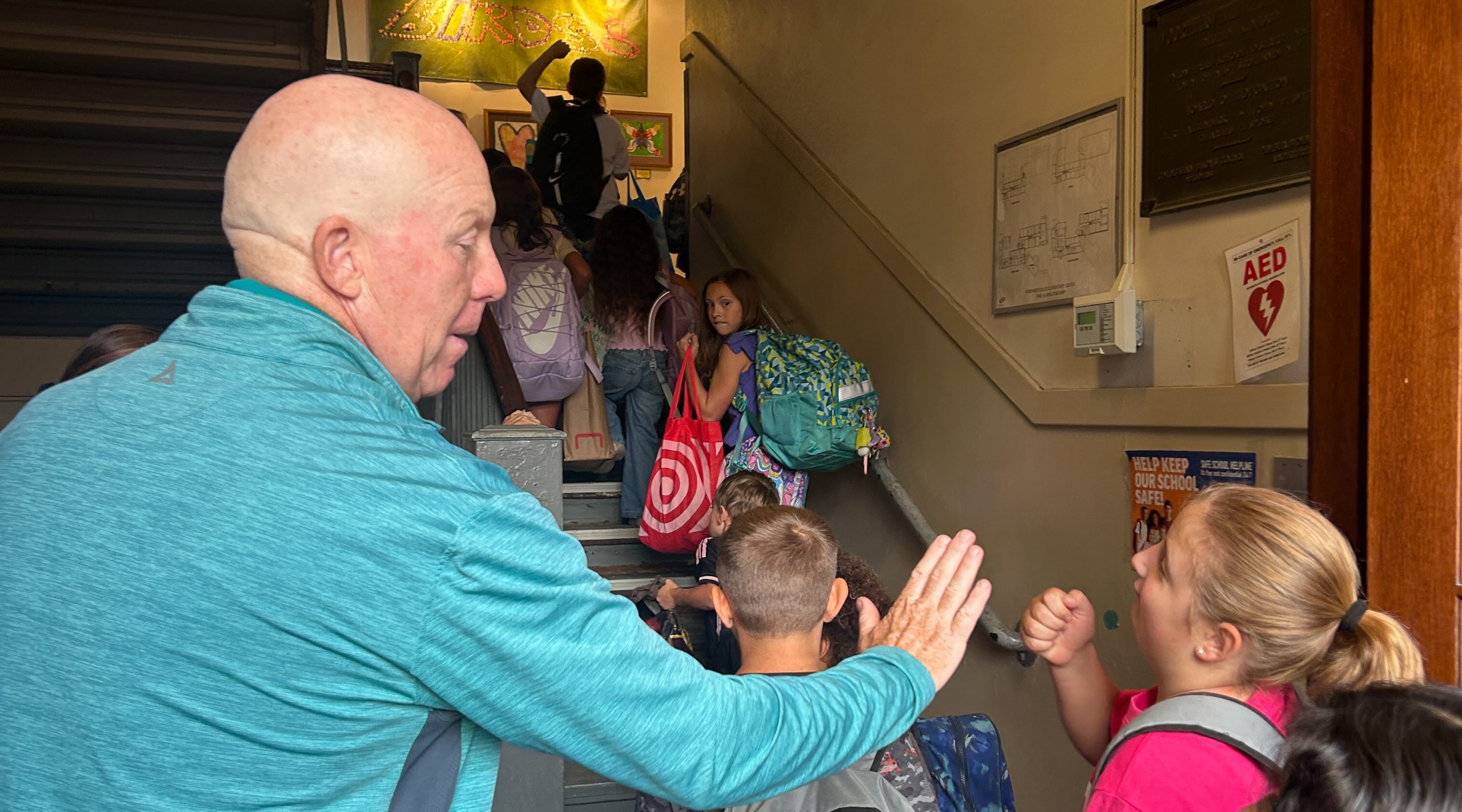 Elementary students ascend stairs. Teacher gives student a high five.