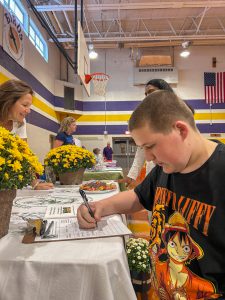 Adults and students talk at Volunteer Fair. One Student signs his name to a sheet.