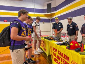 Students, some wearing football jerseys, talk with members of the New Salem Fire Department.