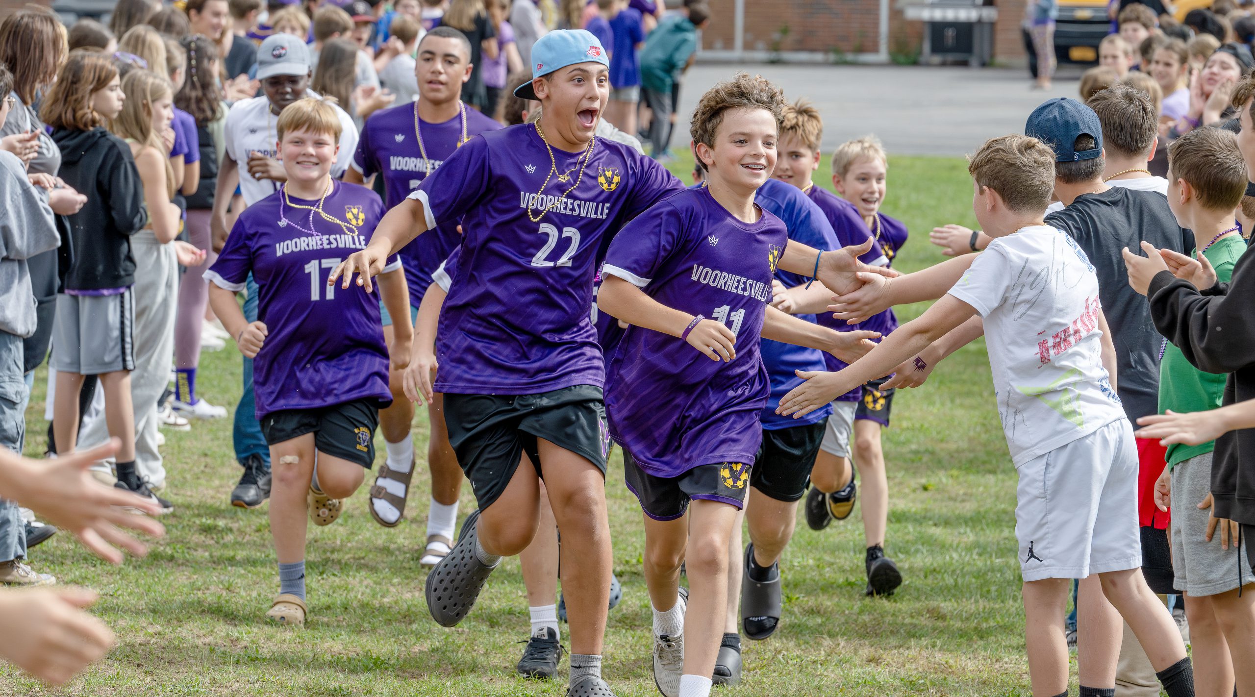 Middle school boys, wearing school jerseys run down and slap hands with the crowd during pep rally.