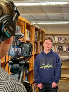 Student delivers lines as a videographer tapes in a library.