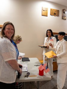 Principal Lisa Cardillo stands at table with two women at naturalization registration.