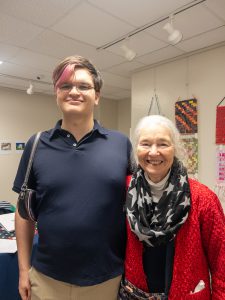 Two attendees pose together and smile inside the venue following the ceremony, with artwork displayed on the walls behind them.