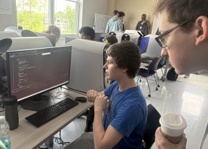 Teen views game coding on desktop monitor.