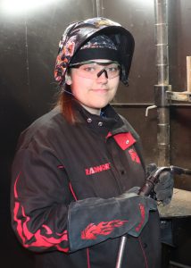 Teen wearing welding hat and goggles holds a welding torch.