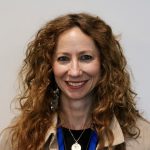 VCSD Board of Education memeber Elizabeth Guastella, who has long wavy hair and is wearing a tan jacket and black t-shirt, smiles warmly for the camera.